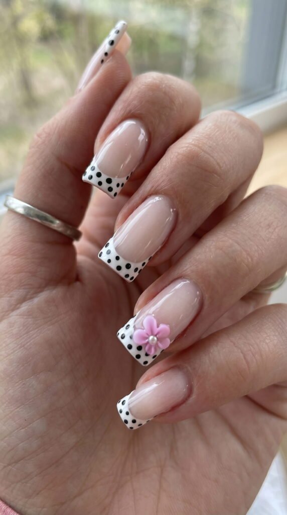 Nude square nails with black polka dot French tips and pink flower accent