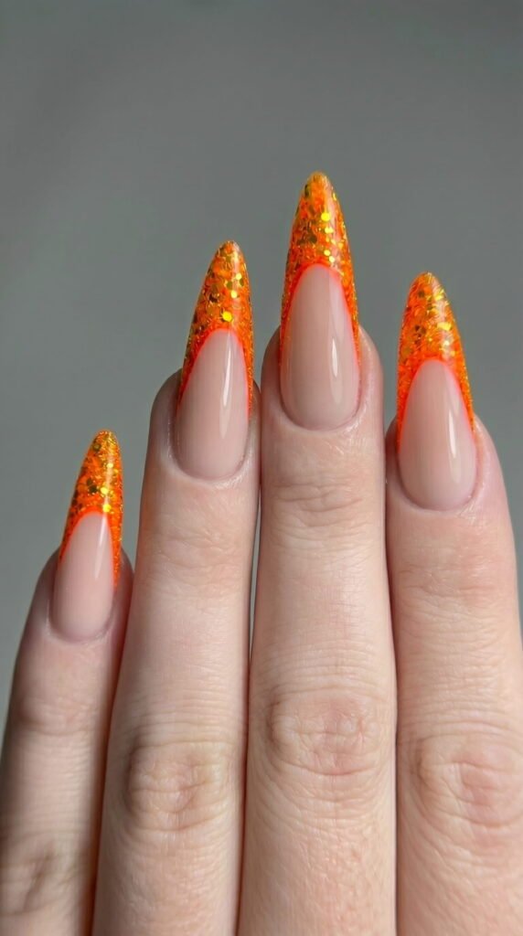 Stiletto nails with milky pink base and orange glitter French tips